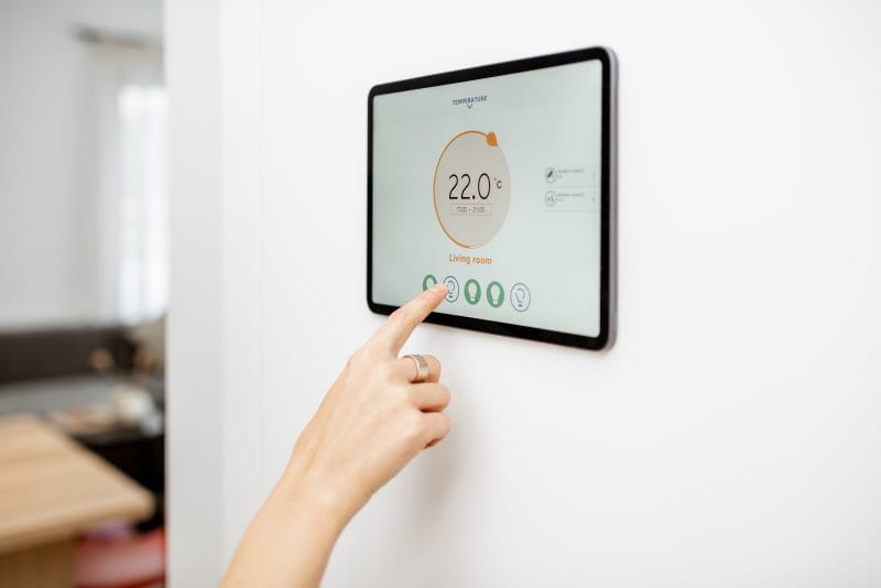 Eine Frauenhand tippt auf einem Tablet an der Wand das Raumklima ein.